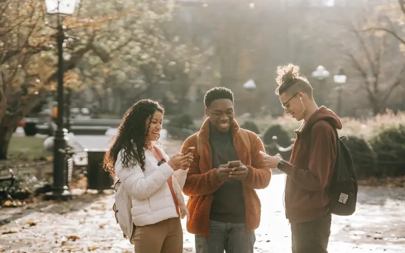 3 young people laughing while doing something on their phones and talking to each other