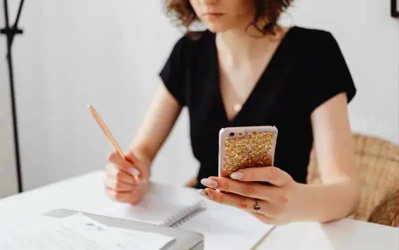 A woman completing a quiz on her smartphone while taking notes.