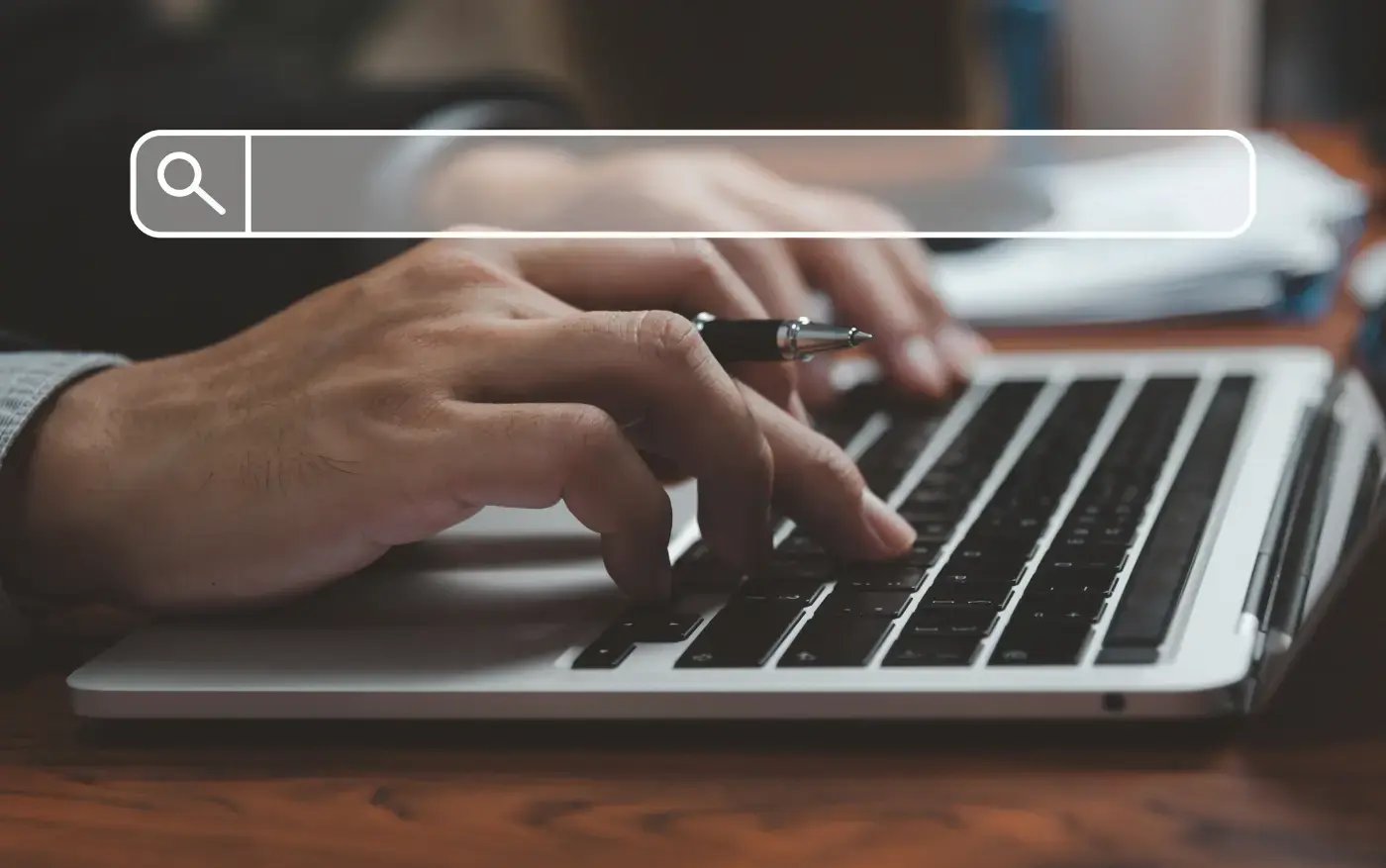 Hände tippen eine Suchanfrage in die Suchleiste eines Laptops.