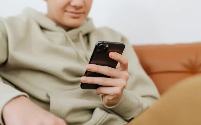 Eine Person entspannt auf dem Sofa und verfolgt auf dem Smartphone einen spannenden Sport-Liveblog.